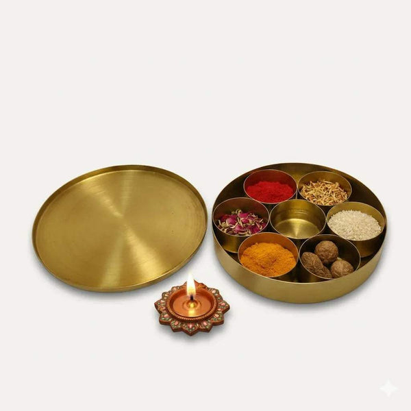 Round brass pooja box lid with open divider tray; diya lamp holder nearby