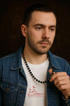 Bead mala necklace on a man’s neck, dark beads with silver flower accents