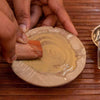 Red sandalwood stick held by a hand over a shallow wooden dish with powder
