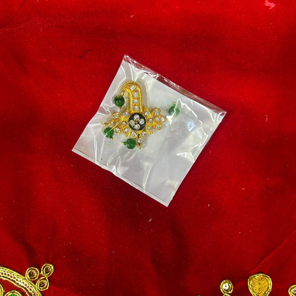 Golden green-stone puja ornament in clear pouch on red fabric