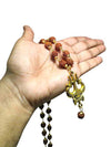 Rudraksha bead mala necklace with gold Trishool pendant, held in an open palm.