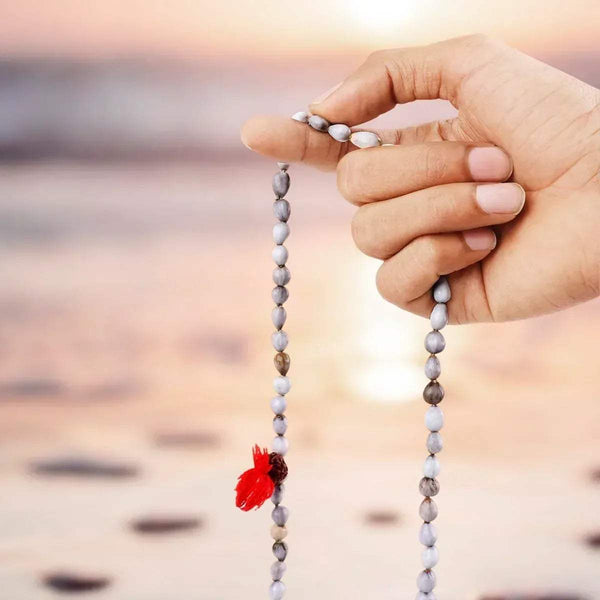 Hand holding off-white bead japa mala with pink tassel