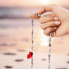 Hands holding a light gray bead mala with pink tassel for chanting