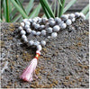 Light gray bead mala with pink tassel lying on textured ground near plants