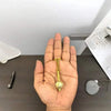 Gold-tone keychain charm held in open palm with chain and locket pendant