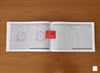 Hindi panchang book open to two pages of grid date tables with red emblem