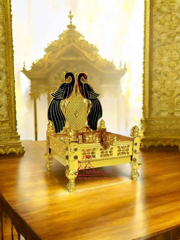 Gold-plated brass singhasan with peacock topper and engraved front panel.