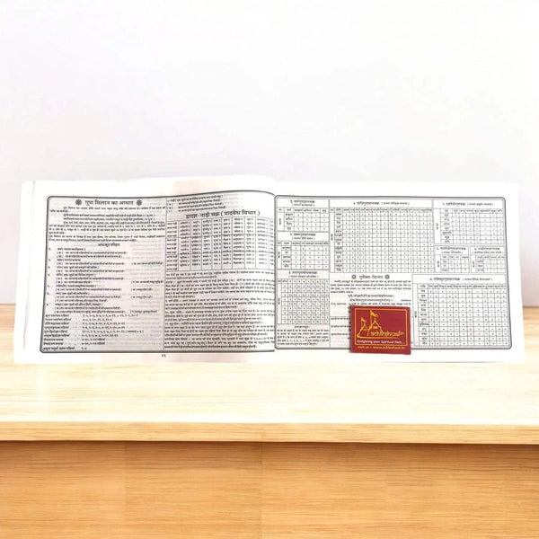 Hindu panchang book open to a chart table layout with red bookmark on lower right
