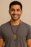 Rudraksha bead mala necklace with gold Trishool pendant, worn on a crew-neck shirt.