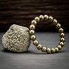 Gold beaded pyrite-style bracelet with spherical metallic beads on a rough stone.