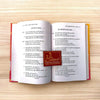 Open Hindi bhajan book with two columns of printed verse and a central emblem.
