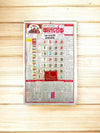 Hindi panchang calendar sheet for 2026 lying on light wood, red date grid