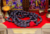 Dark round bead mala with red-orange accents and red tassel on cloth