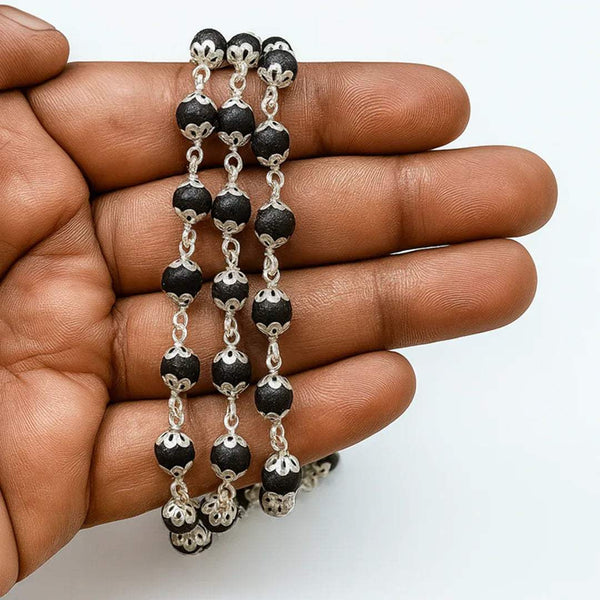 Bead mala necklace strands with dark beads and silver flower charms, held in hand