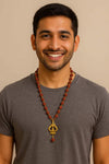 Dark red Rudraksha bead necklace with gold trishool pendant, worn by a smiling man.