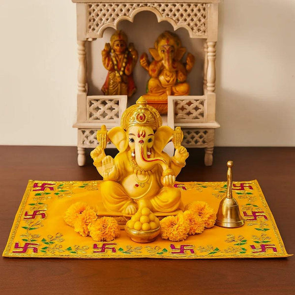 Yellow pooja velvet chowki aasan under deity idols, with decorative border and motifs