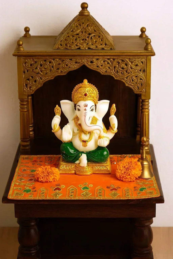 Orange velvet pooja cloth with gold and green embroidered border on a small stand