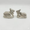 Pair of metal Nandi bull figurines on white background, patterned saddles, silver finish