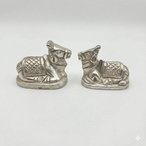 Pair of metal Nandi bull figurines on white background, patterned saddles, silver finish