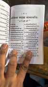 Open stotra book with printed Sanskrit text and hands holding pages
