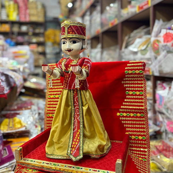 Wooden idol male doll in red-and-gold top and yellow skirt, standing on a red base.