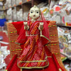 Wooden idol female doll with red veil and crown, red-and-gold dress, hands raised on base.