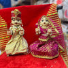 Wooden Radha and Krishna pooja idols in ornate crowns, seated on red base