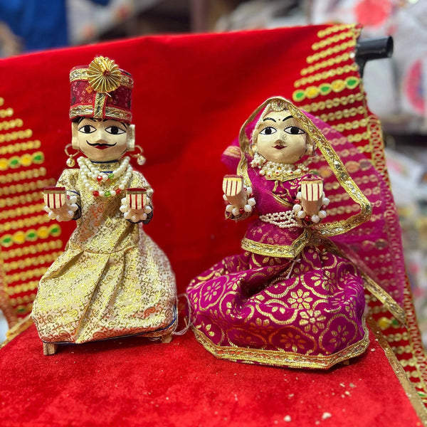 Wooden Radha and Krishna pooja idols in ornate crowns, seated on red base