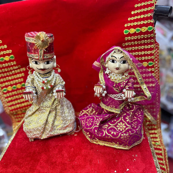 Wooden Radha and Krishna pooja idols, gold-toned outfits on red fabric