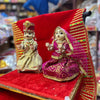 Wooden Radha and Krishna pooja idols, seated on red fabric with gold trim