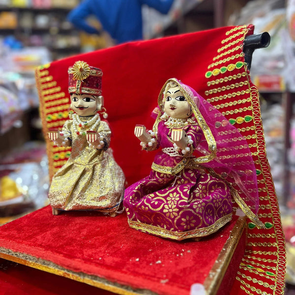 Wooden Radha and Krishna pooja idols, seated on red fabric with gold trim