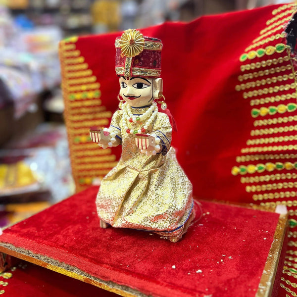 Wooden deity idol figurine of Isar ji, seated with hands raised, gold crown and cream outfit.
