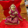 Wooden deity idol figurine with magenta veil and gold trim, seated with outstretched hands.