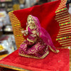 Wooden deity idol figurine in magenta lehenga with draped veil, seated with raised hands.