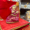 Wooden deity idol figurine in magenta dress with gold trim, seated with hands raised.