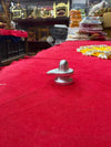 Small metallic shivling ornament with domed top on red cloth