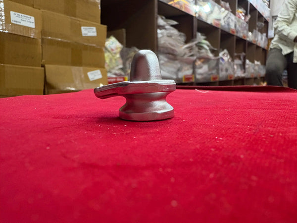 Small metallic shivling ornament on red fabric with rounded base