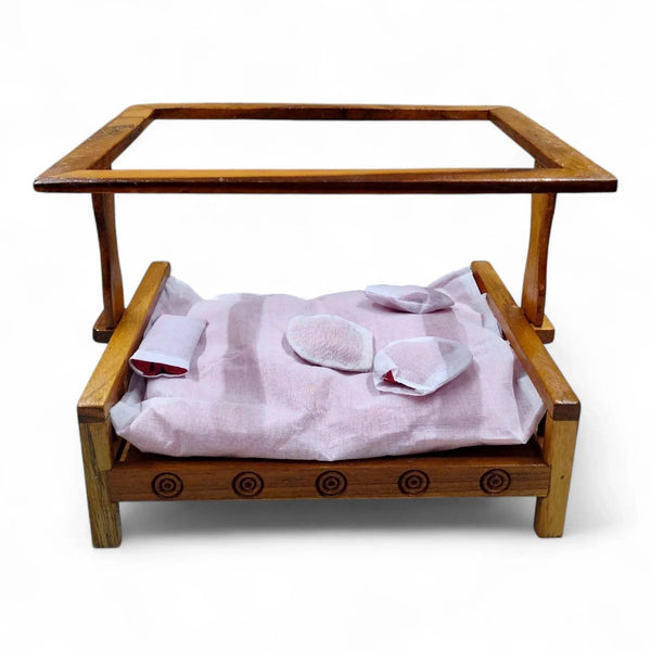 Wooden cot bed with side rails, round carvings along the front, and folded light cloth bedding.