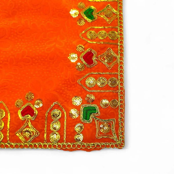 Close-up of orange velvet pooja cloth edge with gold trim and green embroidered motifs