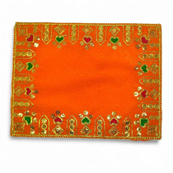 Orange velvet pooja cloth featuring gold, green, and red embroidered corner and edge designs