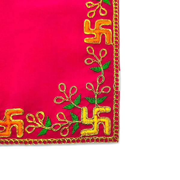 Pink velvet pooja asan corner with green leaves and golden embroidered motif.