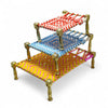 Mini metal charpai beds stacked with red, light-blue, and yellow woven tops