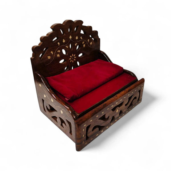 Wooden sofa cum bed with carved frame and red padded seat, angled side view