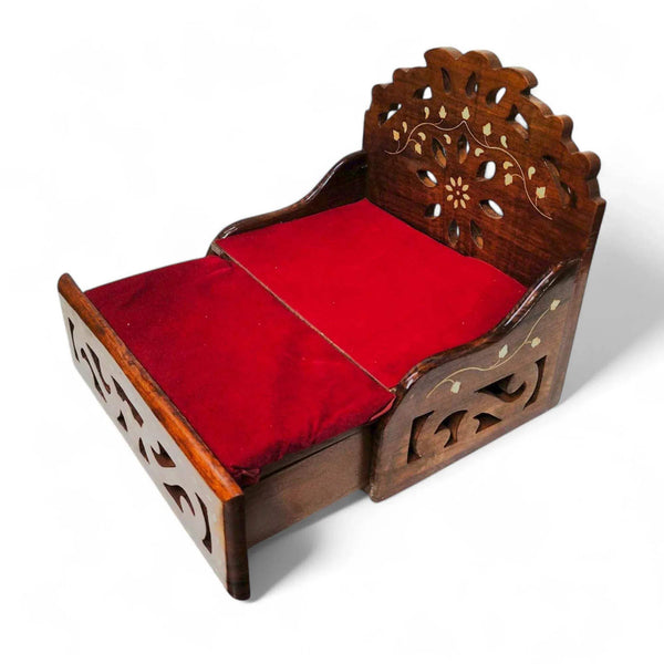 Wooden sofa cum bed with red padded seat and carved side panels, angled view