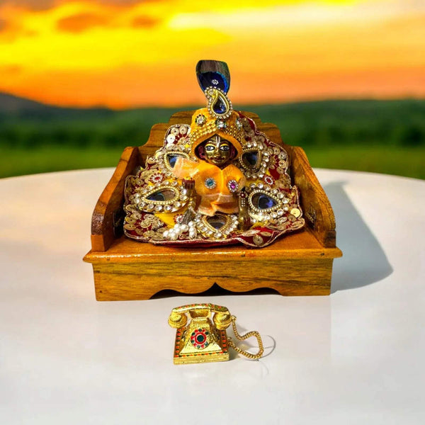 Golden miniature metal telephone toy with gem inlay and gold chain beside wooden base