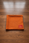 Orange woolen aasan meditation mat with small brand patch near the corner, folded flat.