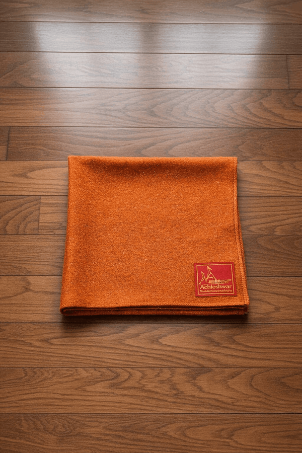 Orange woolen aasan meditation mat with small brand patch near the corner, folded flat.