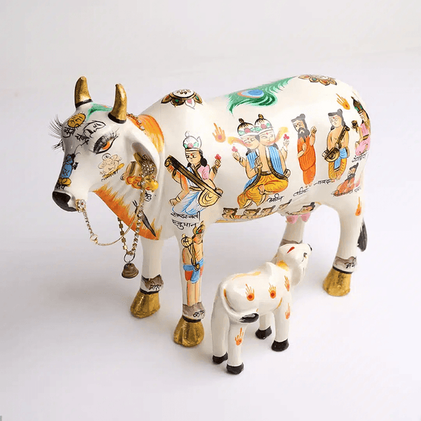 Handcrafted cow idol with calf, white and gold accents, painted deity scenes and bell