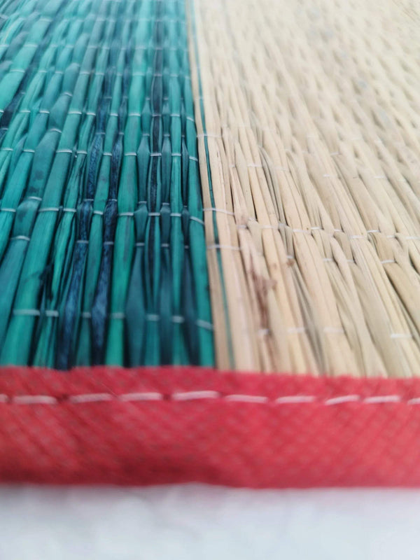 Darbha grass mat corner close-up, teal and beige weave with red stitched trim