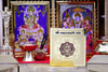 Square gold yantra card on altar shelf, standing between framed deity photos.